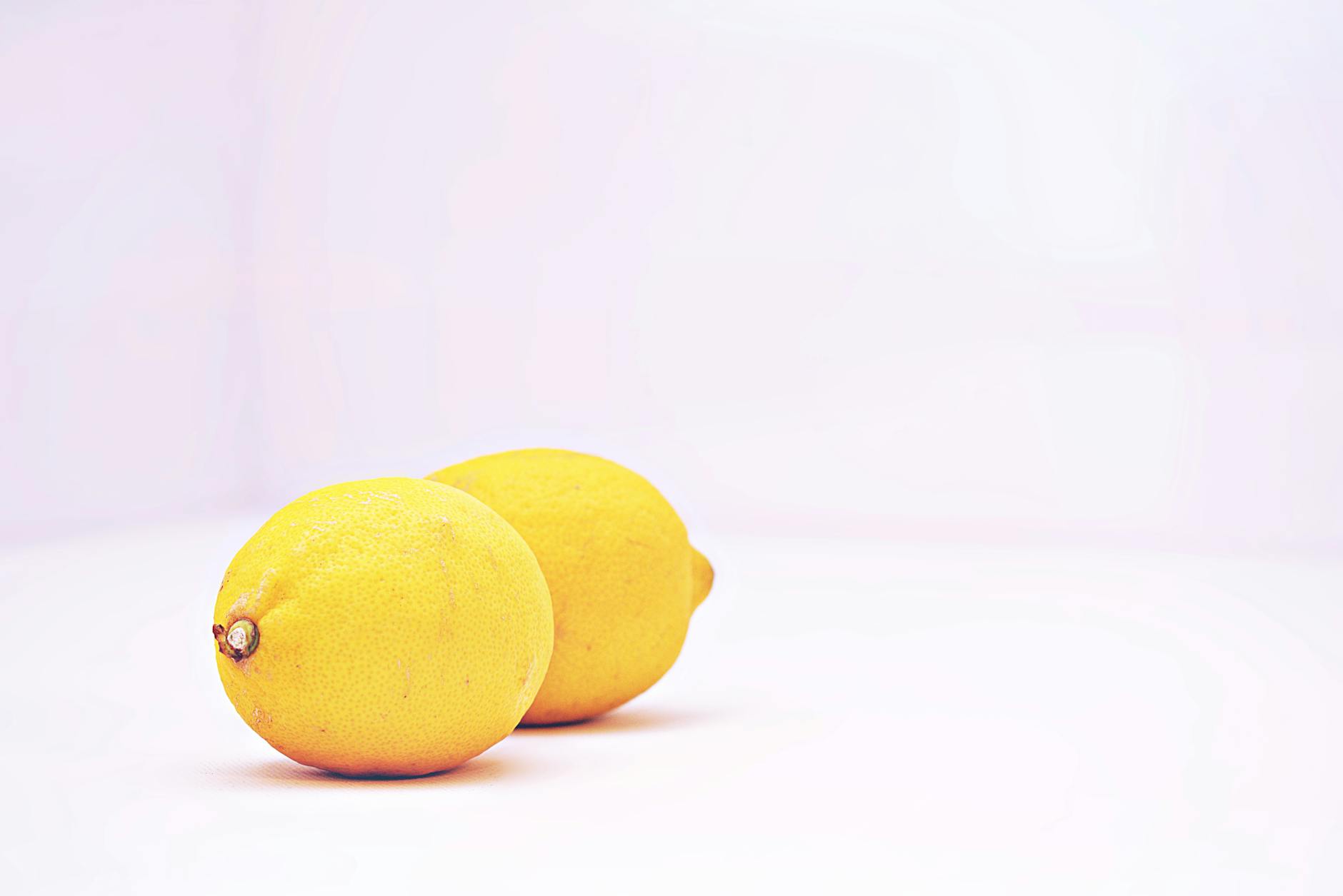 A hand holding a lemon on a soft pink background, symbolizing gentle reconnection and self-discovery.