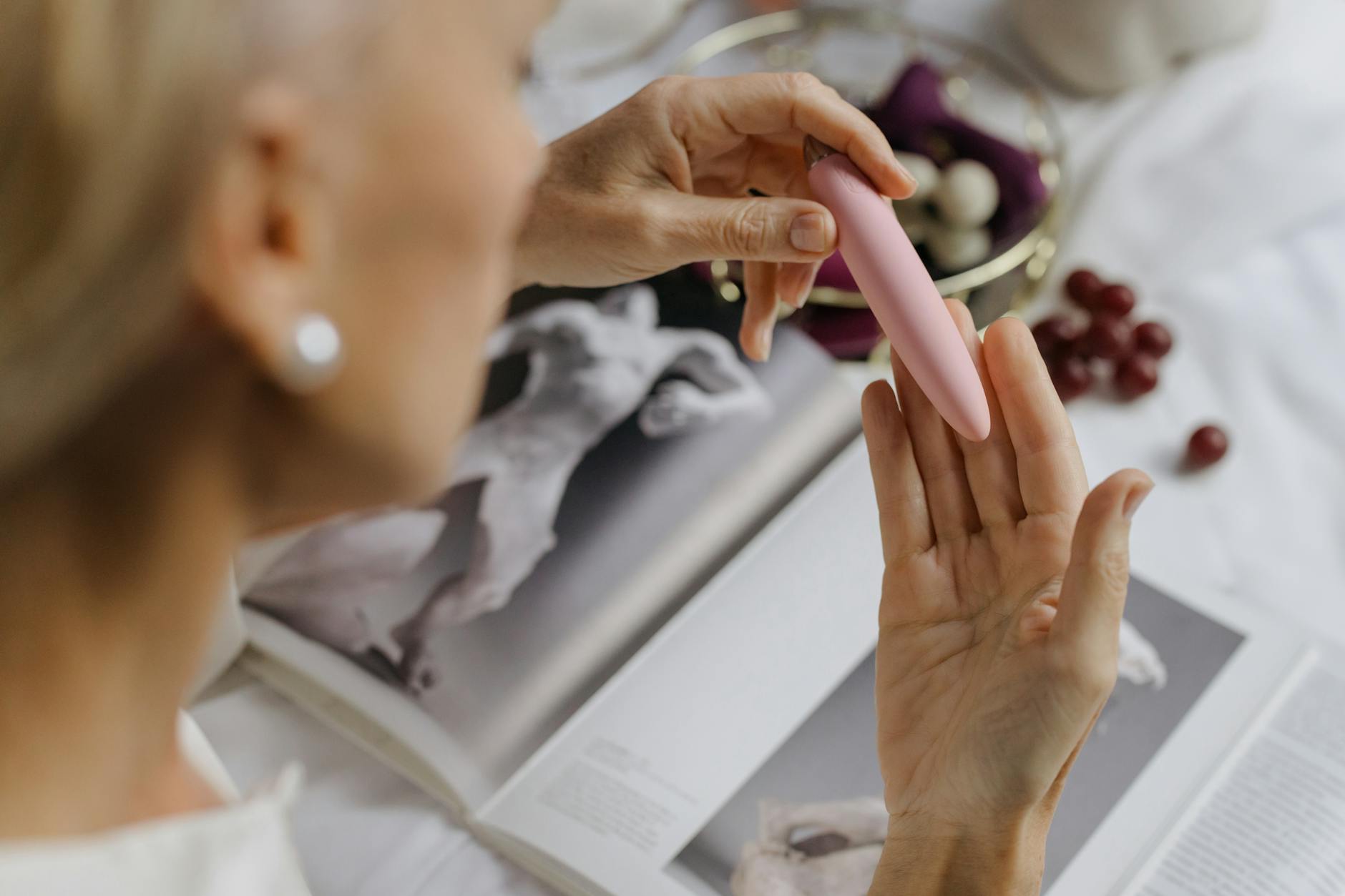 A woman in a contemplative moment, holding a pink vibrator near books about intimacy and personal growth.