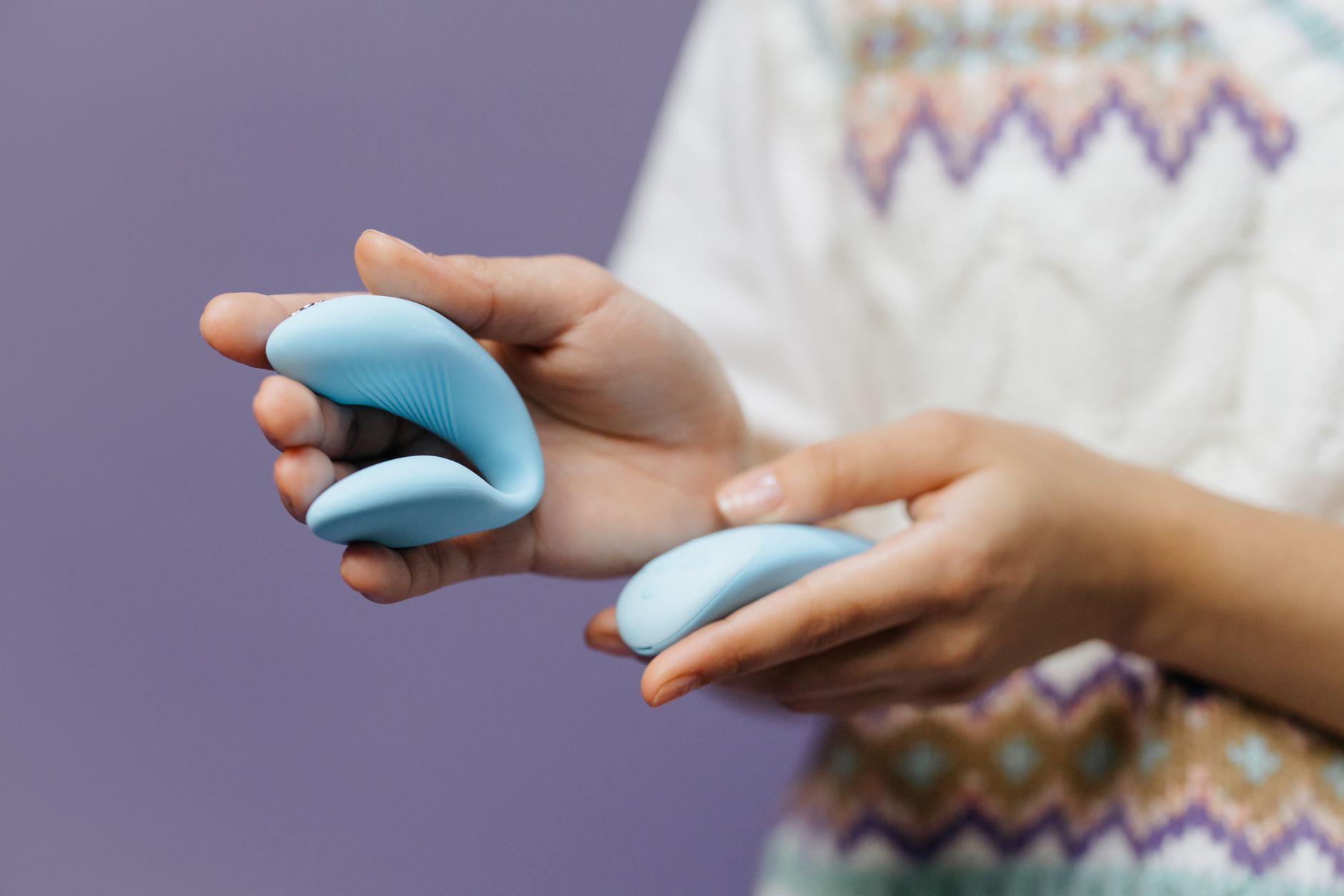 Close-up of hands holding a sleek blue vibrator against purple background, representing intimate exploration during hormonal transitions