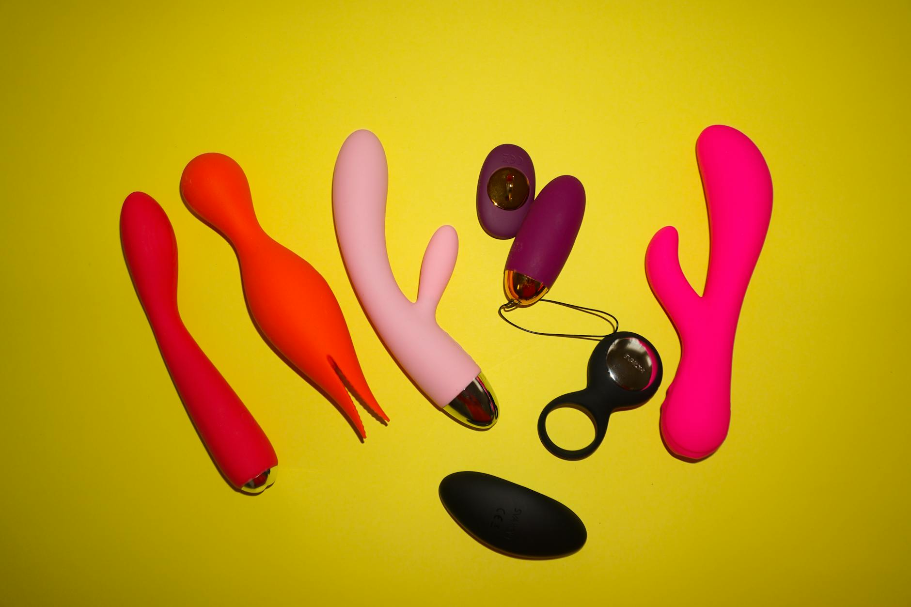 Colorful collection of vibrators and adult toys displayed on a bright yellow background